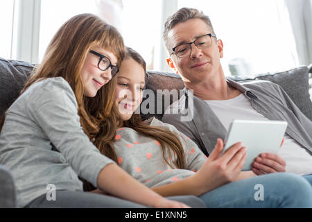 Father and daughters using tablet PC on sofa at home Stock Photo