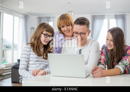 Family of four using laptop together at table in home Stock Photo