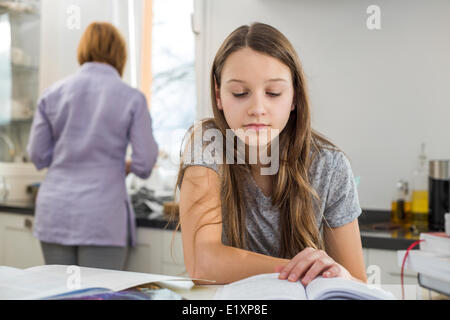 Girl studying at table with mother standing in background Stock Photo