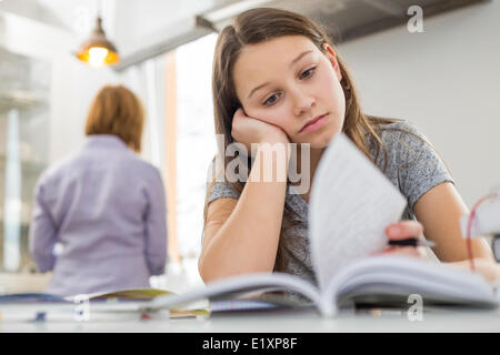 Bored girl studying at table with mother standing in background Stock Photo
