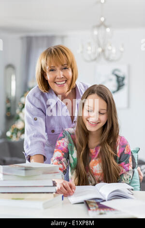 Portrait of happy mother assisting daughter in doing homework at table Stock Photo