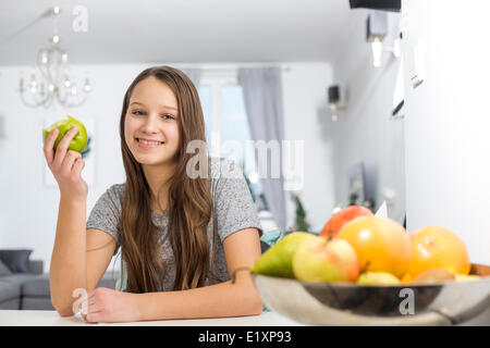 Portrait of smiling girl holding apple while sitting at table in house