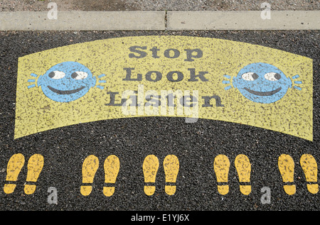 Stop Look Listen sign with smiley faces and footprints painted on a roadside kerb near a primary school road crossing from above. UK Britain Stock Photo