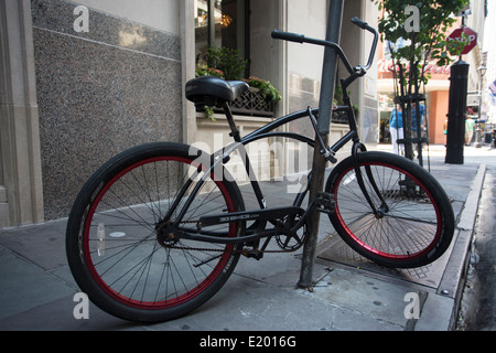 A black bicycle is locked to a pole on an urban street. Stock Photo