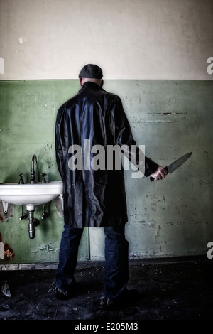 a man in dark clothes with a knife in an abandoned house Stock Photo