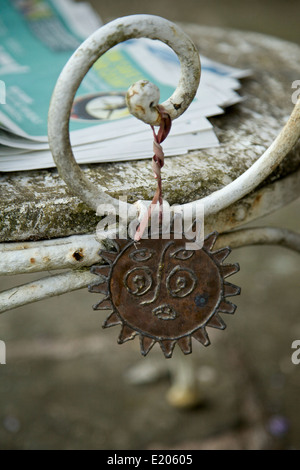 A metal, new-age sculpture hanging from the arm of an old outdoor chair with a copy of a Sunday newspaper on the seat Stock Photo
