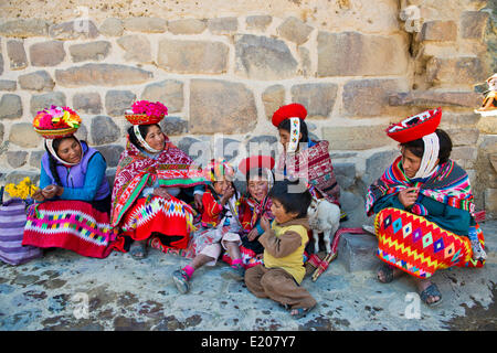 Women and children in traditional dress of the Quechua Indians sitting on the floor in front of a wall, Ollantaytambo Stock Photo