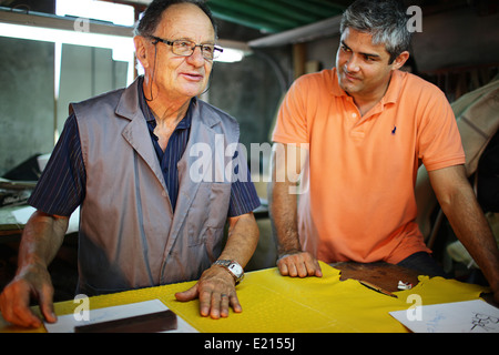 Elderly Italian father and middle aged son pose for a family photo in their workshop. Stock Photo