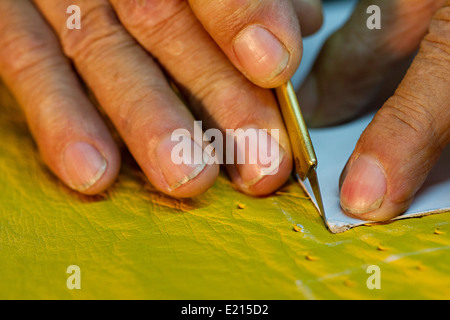 Close up of old mans hands cutting yellow leather with sharp blade Stock Photo