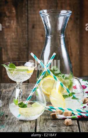 Fresh homemade lemonade with lemon, lime and mint in glasses with vintage cocktail tube over wooden table. Stock Photo