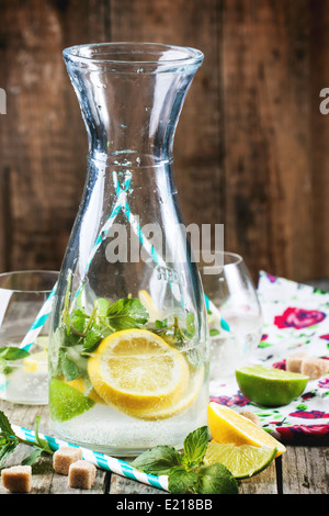 Glass pitcher of homemade lemonade with lemon, lime, sugar and mint on old wooden table. Stock Photo