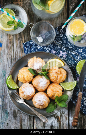 Vintage plate of homemade cakes profiteroles served with lemonade on old wooden table Stock Photo