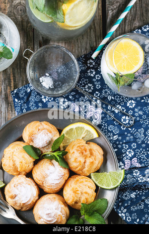 Vintage plate of homemade cakes profiteroles served with lemonade on old wooden table Stock Photo