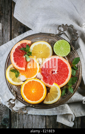 Vintage silver plate with set of sliced citrus fruits lemon, lime, orange, grapefruit over wooden table. Top view. Stock Photo