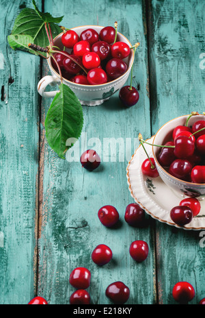 Fresh cherries in vintage tea cups on blue wooden table Stock Photo