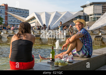 Young man and other people relaxing at Berlin Alexanderplatz in the evening light with a bottle of wine, Germany Stock Photo