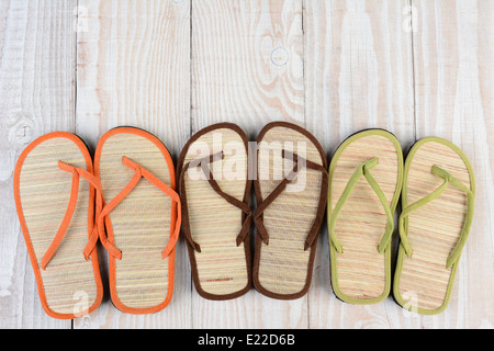 High angle shot of a group of summer beach sandals on a wooden deck. The mulit-colored sandals are lined up in a row by pair. Stock Photo