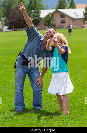 Father & young daughter flying a kite on a grassy field Stock Photo