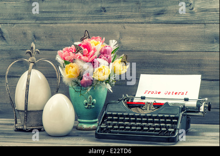 Easter decoration with tulips, eggs and antique typewriter. Sample text Happy Easter! in german. Vintage style toned picture Stock Photo