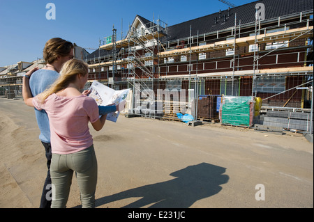 Young couple with blueprint is looking at newly built houses on construction site Stock Photo