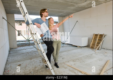 Young couple with blueprint is looking how their new home is being built Stock Photo