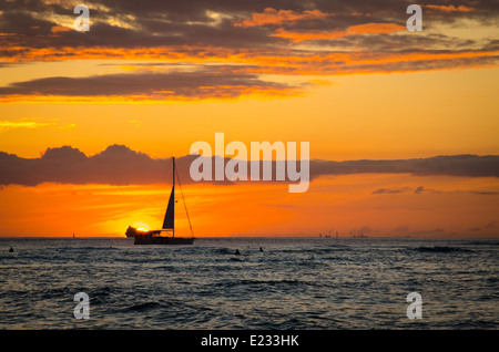 Boat silhouetted in front of the setting sun seen from Waikiki Beach in Hawaii Stock Photo
