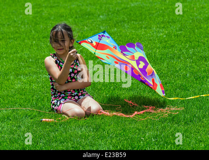 Young hispanic girl flying a kite on a grassy field Stock Photo