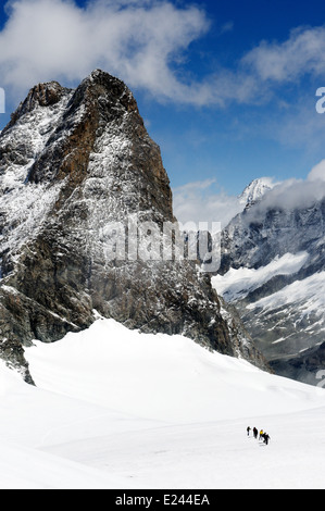 Figures of a mountaineering group high on Pigne d'Arolla near the Vignettes hut in the Swiss Alps, with L'Eveque beyond Stock Photo