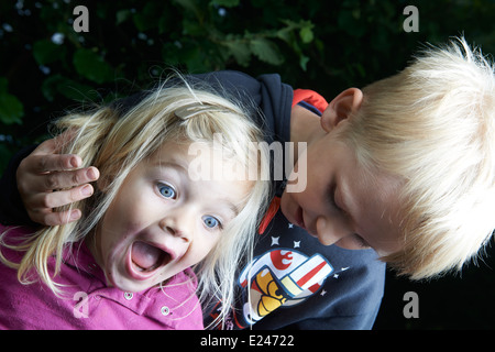 A brother teasing his little sister outside in summer yard Stock Photo