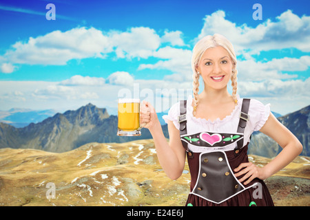 Beautiful Bavarian woman holding a pint of beer somewhere high in the mountains Stock Photo
