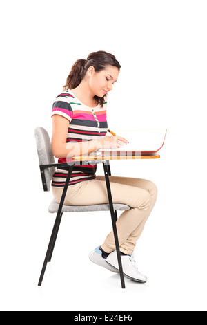 Female student writing in a notebook seated on a school desk Stock Photo