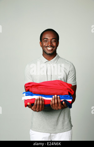 Portrait of a cheerful african man holding his clothes on gray background Stock Photo