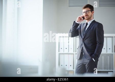 Handsome businessman in suit and eyeglasses speaking on the phone in office Stock Photo