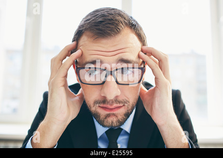 Frustrated businessman in eyeglasses touching his head Stock Photo