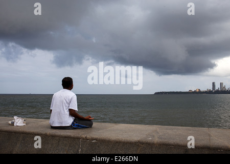A man practising yoga and meditating on the footpath sea promenade along Marine Drive in Mumbai, India. Stock Photo