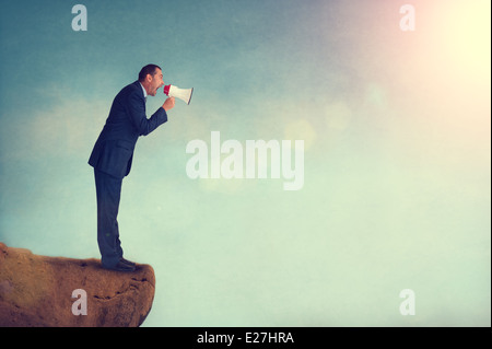 businessman shouting through a megaphone from a cliff or mountain edge Stock Photo