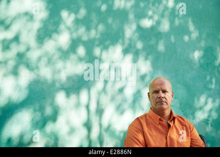 Portrait of mature caucasian man with orange shirt sitting in park and looking at camera with sad expression Stock Photo
