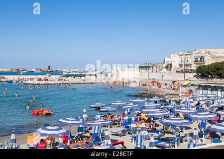 Beach parasols on a crowded sunny beach in summer sunshine on the coast at Otranto, Puglia, Salento region of southern Italy Stock Photo