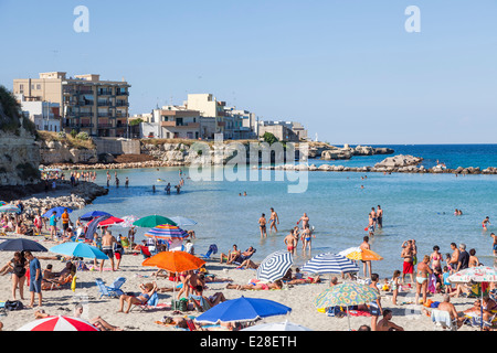 Beach parasols on a crowded sunny beach in summer sunshine on the coast at Otranto, Puglia, Salento region of southern Italy Stock Photo