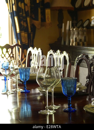 A shiny wooden dining table set with plates and glassware, including blue glasses. Stock Photo