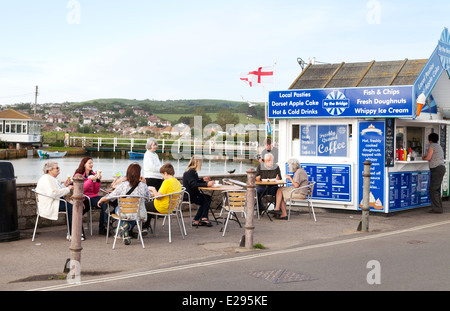 People eating fish and chips at a fish and chip shop, West Bay, Bridport Harbour, Dorset coast, England UK Stock Photo