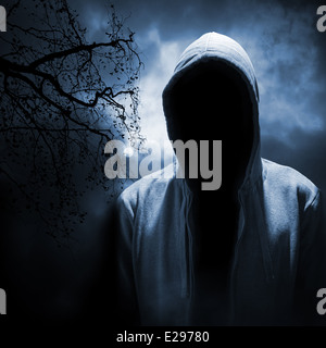 Dangerous man hiding under the hood in the dark night forest Stock Photo