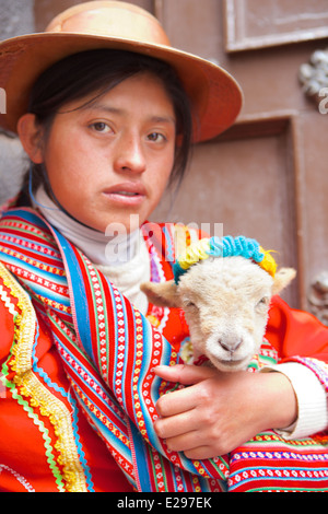 A portrait of a Quechua girl in traditional native dress holding a lamb in Cusco in the Andes, Peru, South America Stock Photo