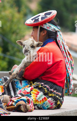 A portrait of a young Quechua woman in traditional native dress holding a lamb in Cusco, Andes, Peru, South America Stock Photo