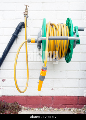 A garden hose reel with yellow kink resisting hose wall mounted for convenient deployment Stock Photo