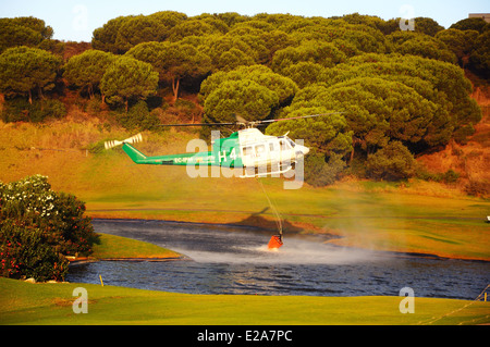 Bell 412 registration EC-IPM collecting water for fire fighting from a golf club lake, Cabopino Golf, Spain, Western Europe. Stock Photo