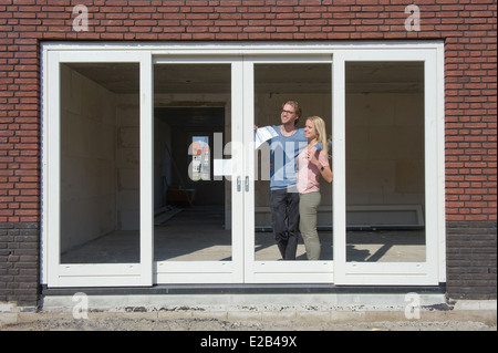 Young couple with blueprint is looking happily outside to the view from their new home Stock Photo