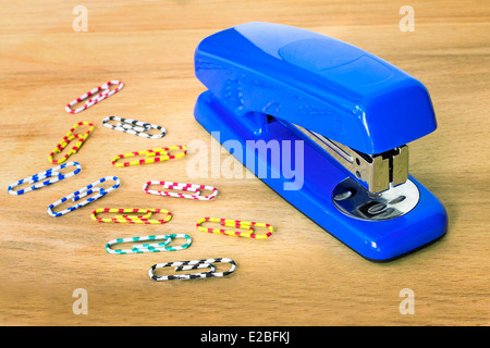 Bright the blue stapler and multi-colored paper clips lie on a table. Stock Photo