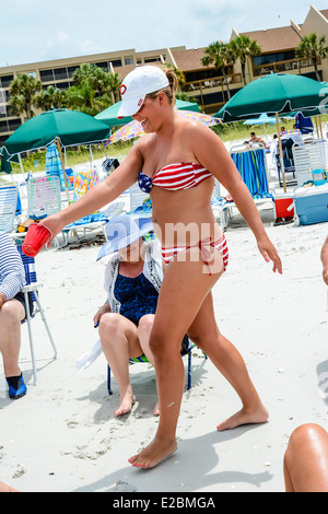 Woman wears patriotic stars and stripes bikini on the beach amongst family & friends celebrating the 4th of July, USA Stock Photo