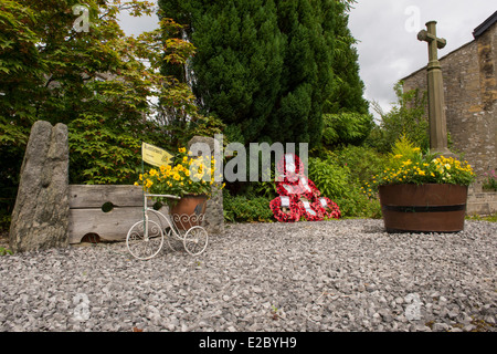 Small quiet attractive garden with stone war memorial, poppy wreaths, flowers in planters & village stocks - Kettlewell, Yorkshire Dales, England, UK. Stock Photo